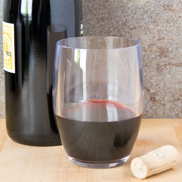 A customizable stemless plastic wine glass filled with red wine next to a bottle.