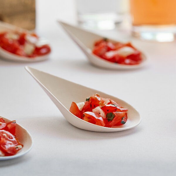 A table with several EcoChoice compostable sugarcane taster spoons filled with tomatoes on it.