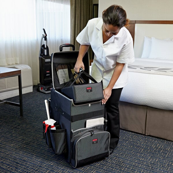 A woman in a white coat using a Rubbermaid Large Executive Quick Cart to put a suitcase in a bag in a hotel room.