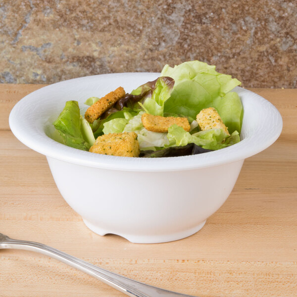 A white GET textured melamine bowl filled with salad, lettuce, and croutons with a fork.