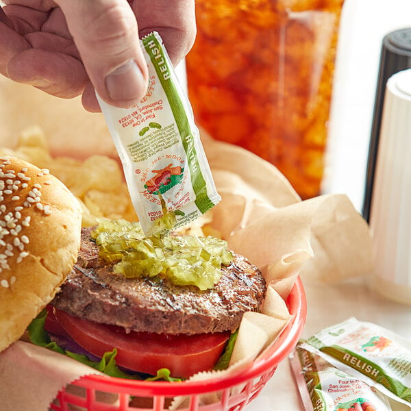 A hand putting a Relish packet on a burger.