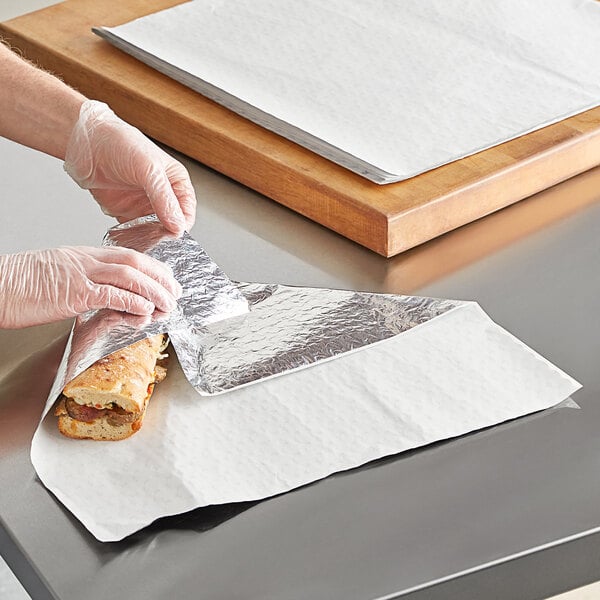 A person wearing plastic gloves wrapping a sandwich in a Choice insulated foil wrapper.