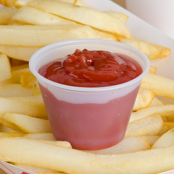 A Solo translucent polystyrene souffle cup of ketchup on a plate of french fries.