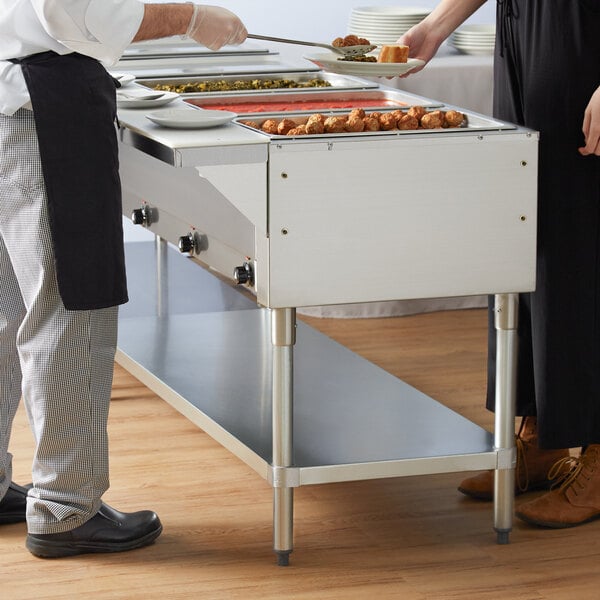 A man and woman serving food from an Advance Tabco electric steam table on an outdoor buffet table.