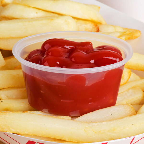 A clear oval plastic container with a lid of french fries with a plastic container of ketchup.