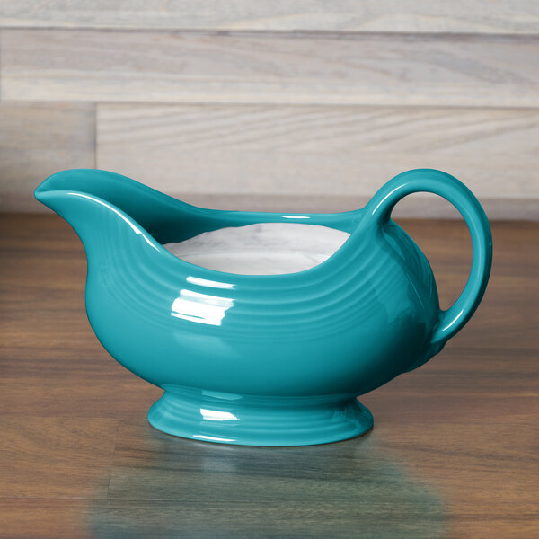 A turquoise Fiesta gravy boat on a wood surface.