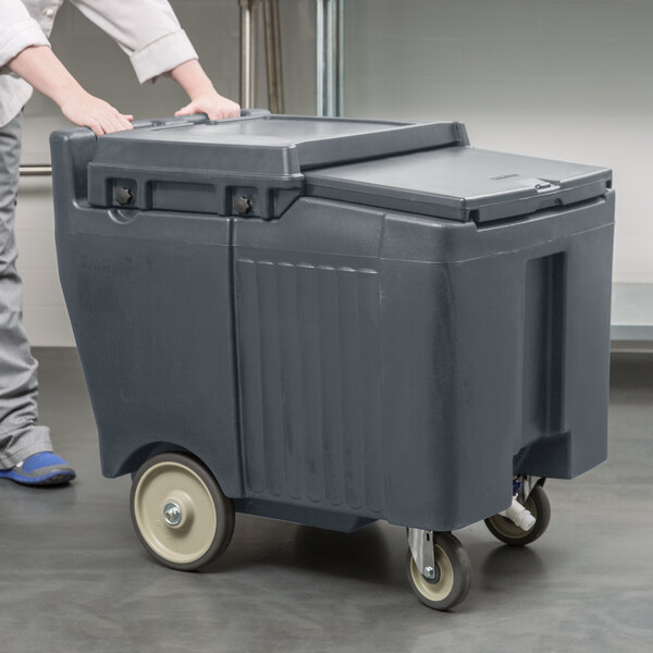 A person pushing a Cambro Granite Gray Mobile Ice Bin on wheels.