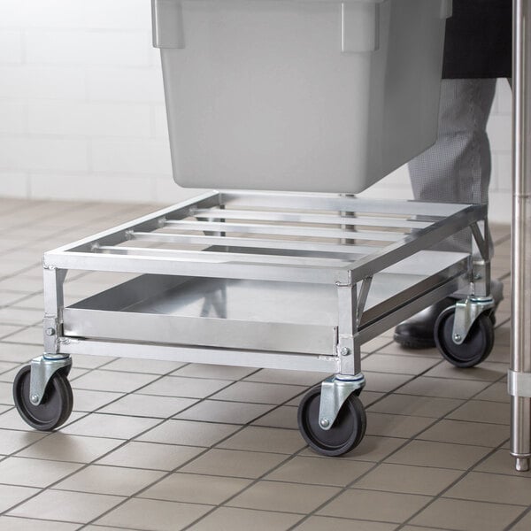 A person pushing a metal container on a Channel SPCD-A Aluminum Poultry Crate Dolly.