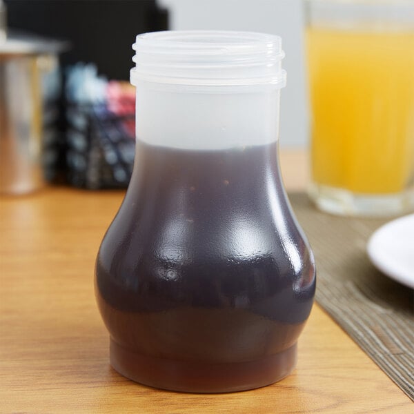 A Tablecraft polypropylene jar filled with brown liquid sitting on a table.