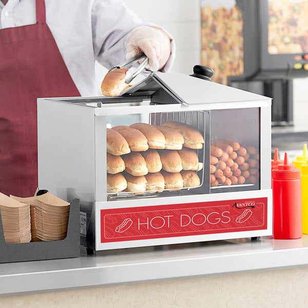 A person putting hot dogs into an Avantco hot dog machine.