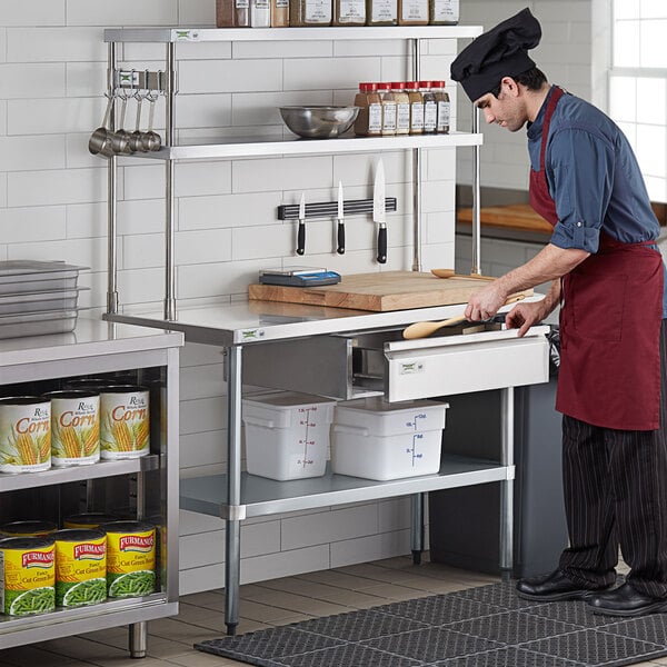 A man in a chef's uniform using a Regency stainless steel table mounted double deck overshelf.