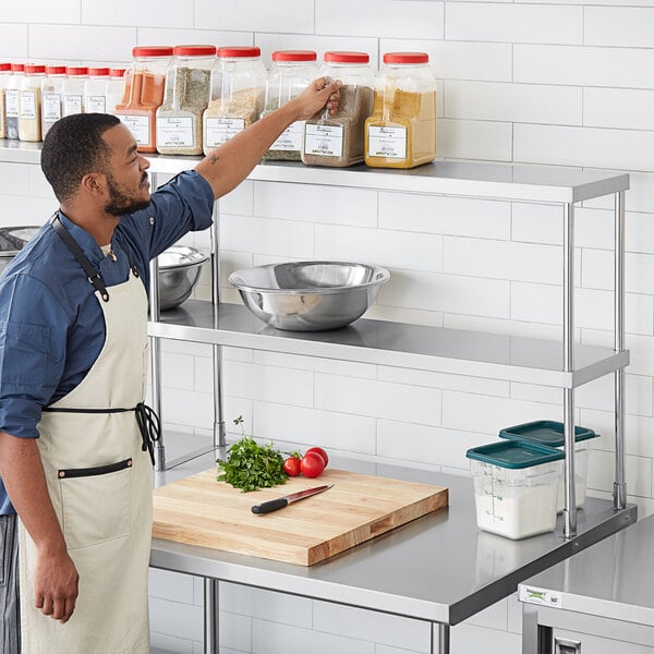 A man in an apron using a Regency double deck overshelf in a professional kitchen.
