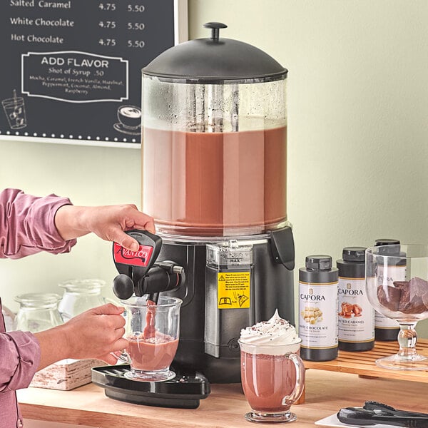 A woman using an Avantco hot beverage dispenser to pour hot chocolate into a glass.