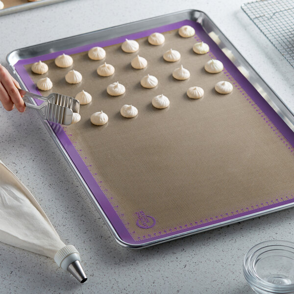 A person using a Mercer Culinary purple silicone baking mat to make small white cookies with a cookie cutter.