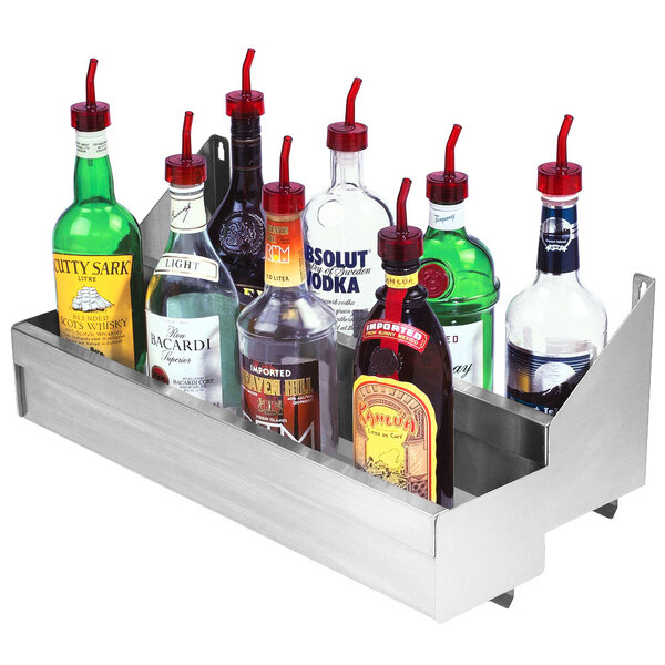 A stainless steel double tier speed rail on a counter with bottles of alcohol.
