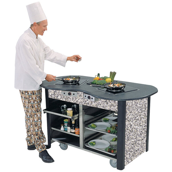 A chef standing next to a Lakeside stainless steel induction cooking cart in a professional kitchen.
