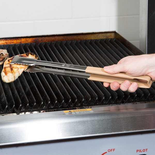 A person using Vollrath tan-coated tongs to cook food on a grill.