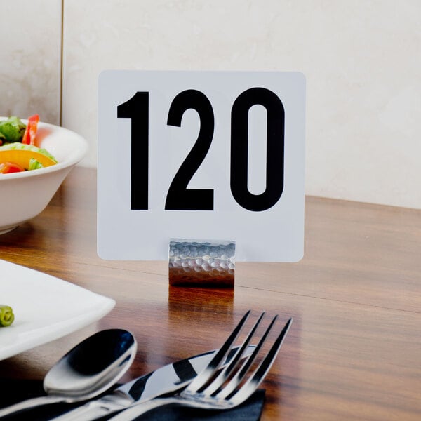 An American Metalcraft hammered aluminum cylinder table card holder with a number in it.