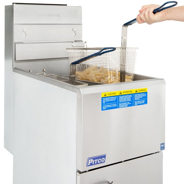 A person using a blue fryer basket to fry fries in a Pitco gas fryer.