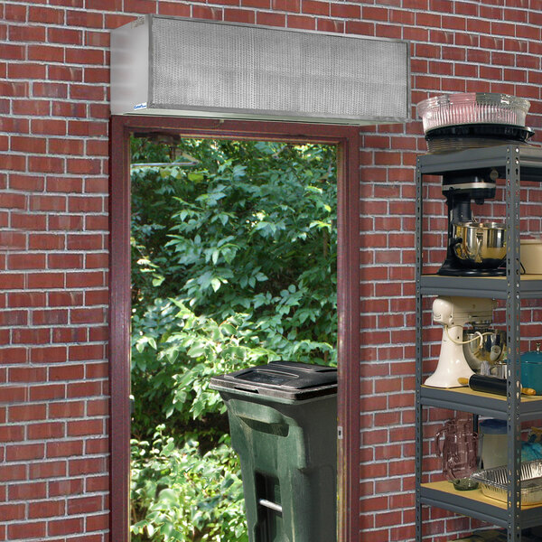 A door is open to a brick wall with a window and a shelf with food items.