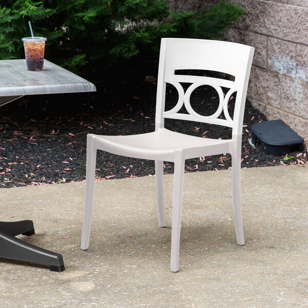 A Grosfillex white plastic stacking chair on a concrete patio.