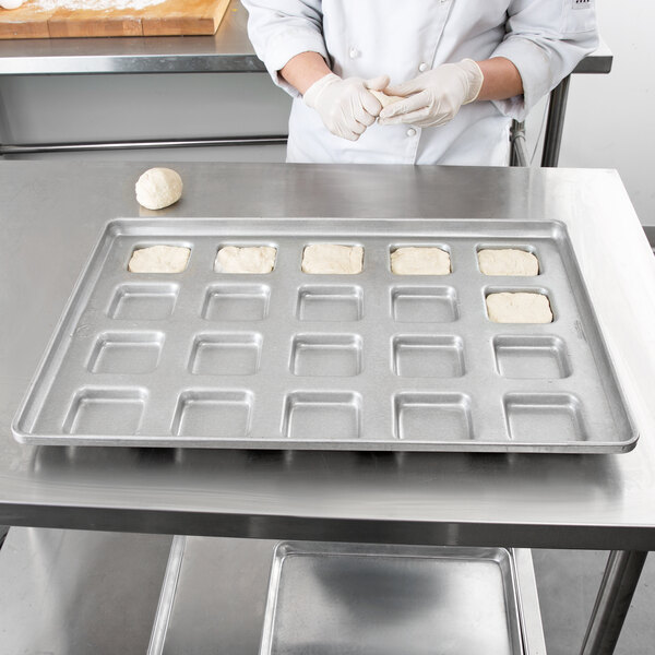 A person in a white chef's uniform using a Chicago Metallic square ciabatta roll pan to bake dough.