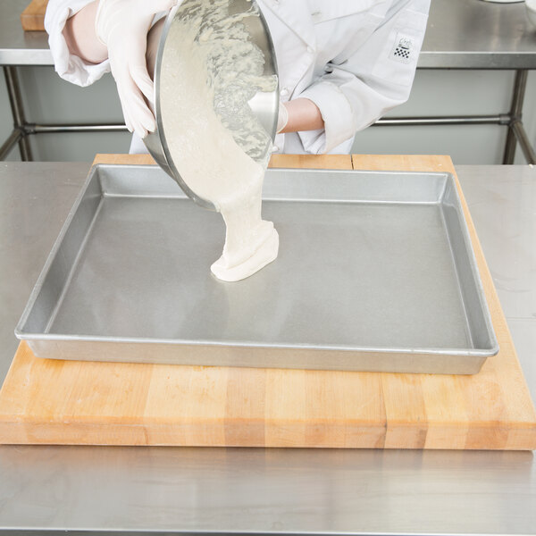 A person pouring white liquid into a Chicago Metallic aluminized steel sheet cake pan.