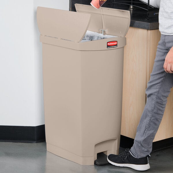 A person using a Rubbermaid Slim Jim tan end step-on trash can.