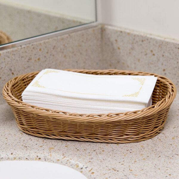 A wicker basket of Lavex Linen-Feel Royal paper guest towels on a counter.