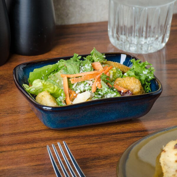 A blue Tuxton rectangular bowl filled with salad on a table.