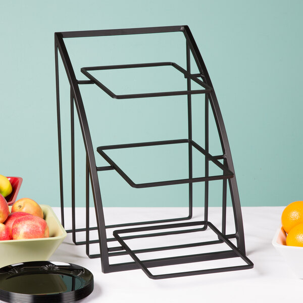 A black metal Cal-Mil display stand with bowls of fruit on it.