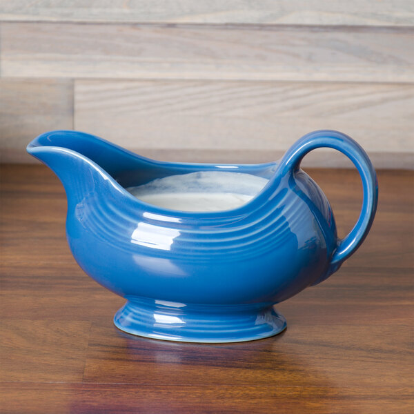 A blue Fiesta gravy boat with white liquid on a wood surface.