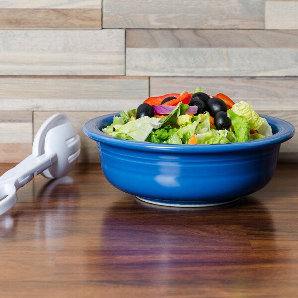 A blue Fiesta serving bowl filled with salad on a wooden table.