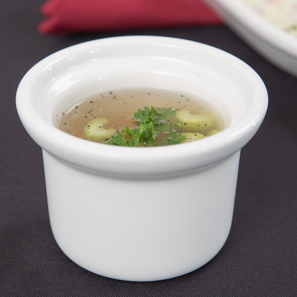 A Tuxton white china bowl filled with soup and greens.