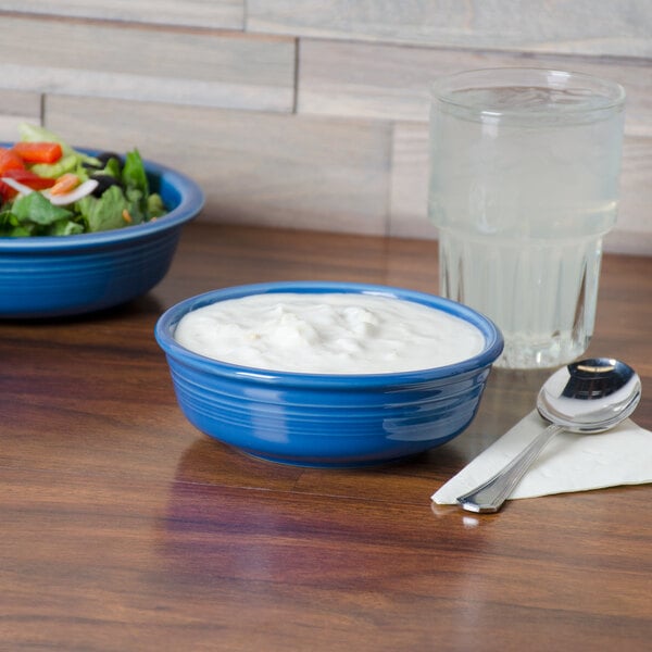 A blue Fiesta china bowl filled with yogurt and salad on a table.