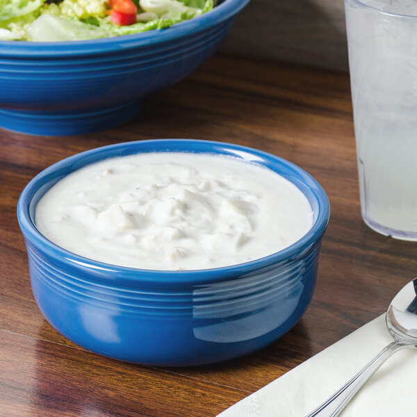 A blue Fiesta chowder bowl with white liquid in it on a table with salad.
