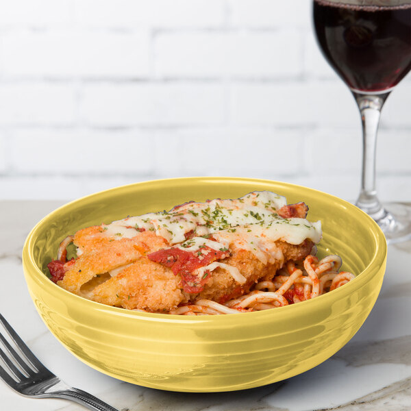 A Fiesta sunflower yellow bowl filled with spaghetti and meatballs on a table with a glass of red wine.