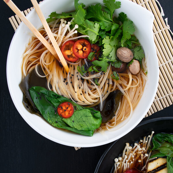 A bowl of noodles with Kikkoman soy sauce and vegetables on a white background.