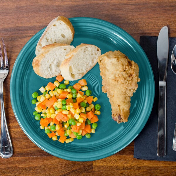 A Fiesta turquoise china plate with food, bread, a fork, and a knife.