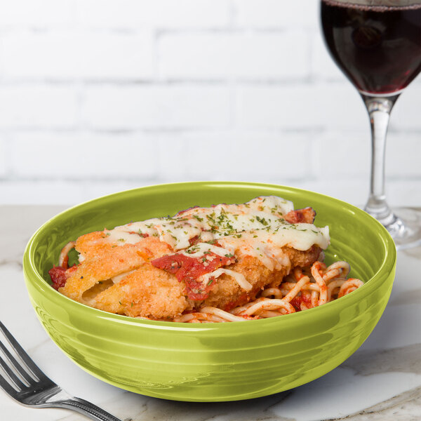 A Fiesta lemongrass medium bistro bowl filled with food on a table with a glass of wine.
