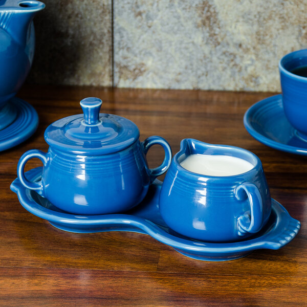A Fiesta Lapis china sugar and creamer tray set on a wooden surface.