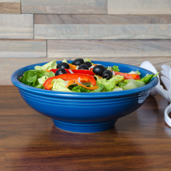 A blue Fiesta pedestal bowl filled with salad on a table.