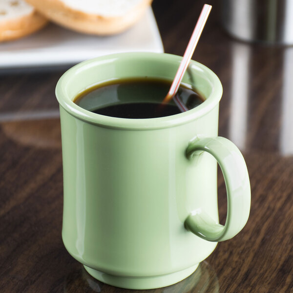 A GET Diamond Harvest avocado mug filled with coffee and a straw on a table.