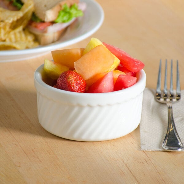 A bowl of fruit next to a sandwich on a table.