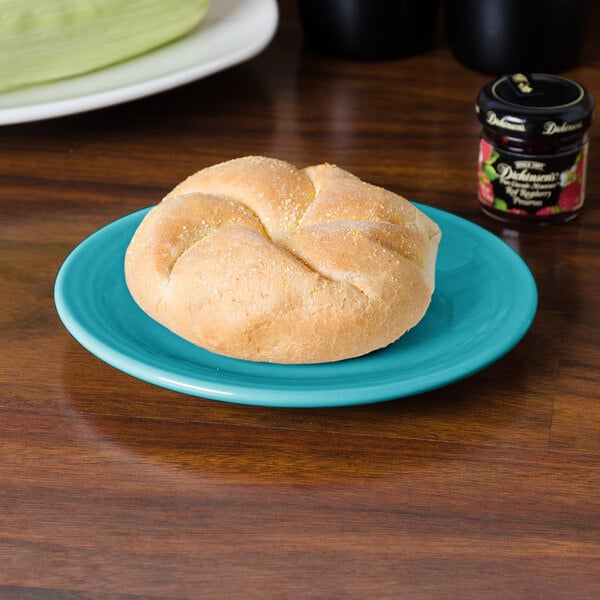 A Fiesta® turquoise bread and butter plate with a roll on it.