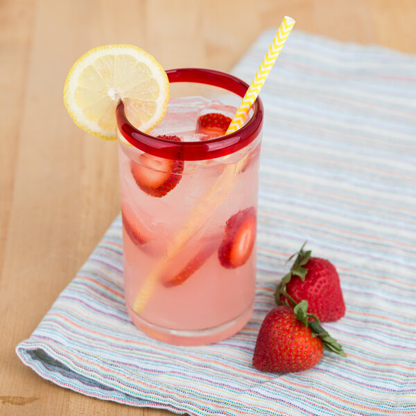 A Libbey Aruba cooler glass with a red rim filled with a pink drink and a straw with strawberries.