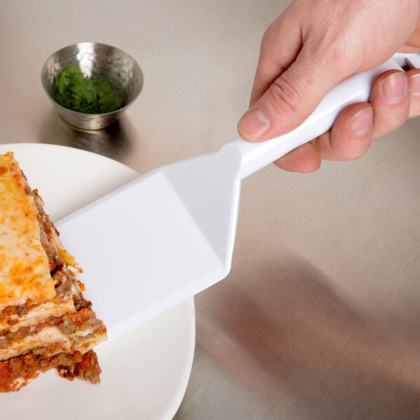 A hand holding a Fineline white disposable spatula over a plate of lasagna.