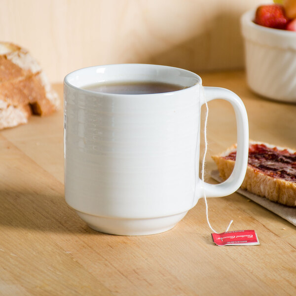 A Tuxton bright white china mug filled with tea and a tea bag on a table.