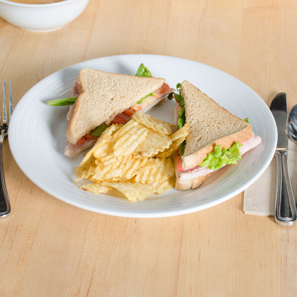 A Tuxton Pacifica bright white china plate with a sandwich and chips on it.