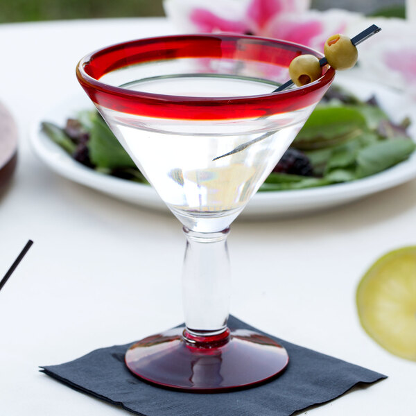 A Libbey martini glass with a red rim and base filled with a drink and olives.